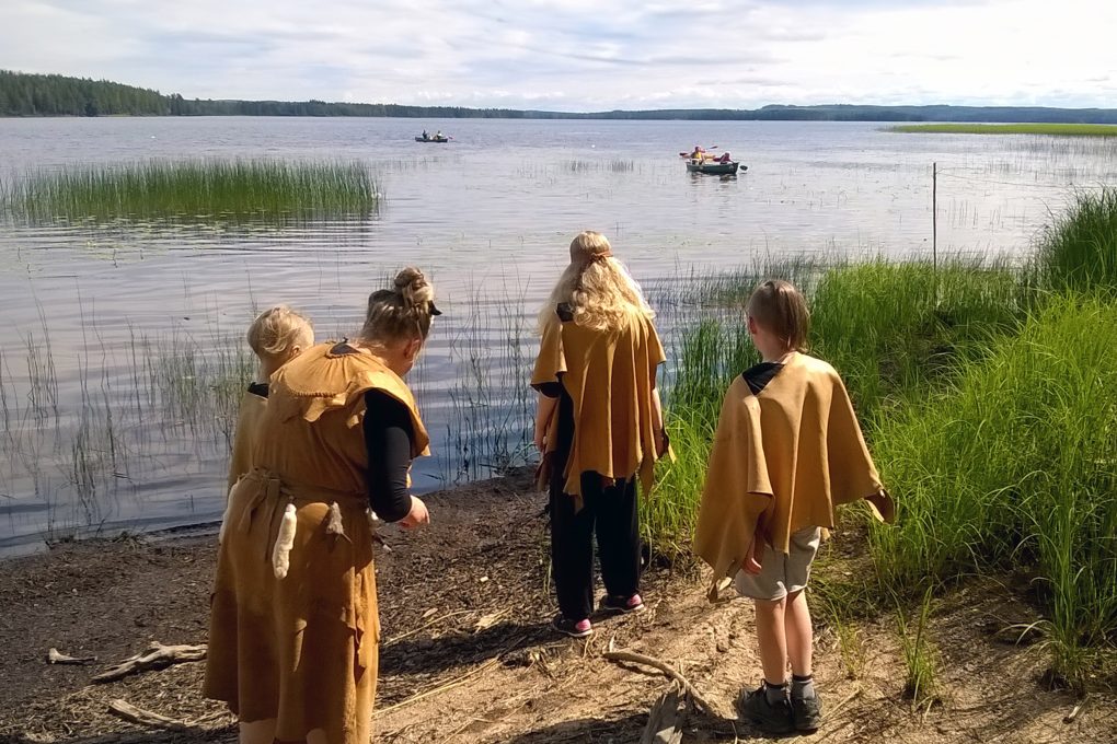 Lapsia ja Kivikauden kylän opas kohteen rannalla. Kuva: Saarijärven museo.